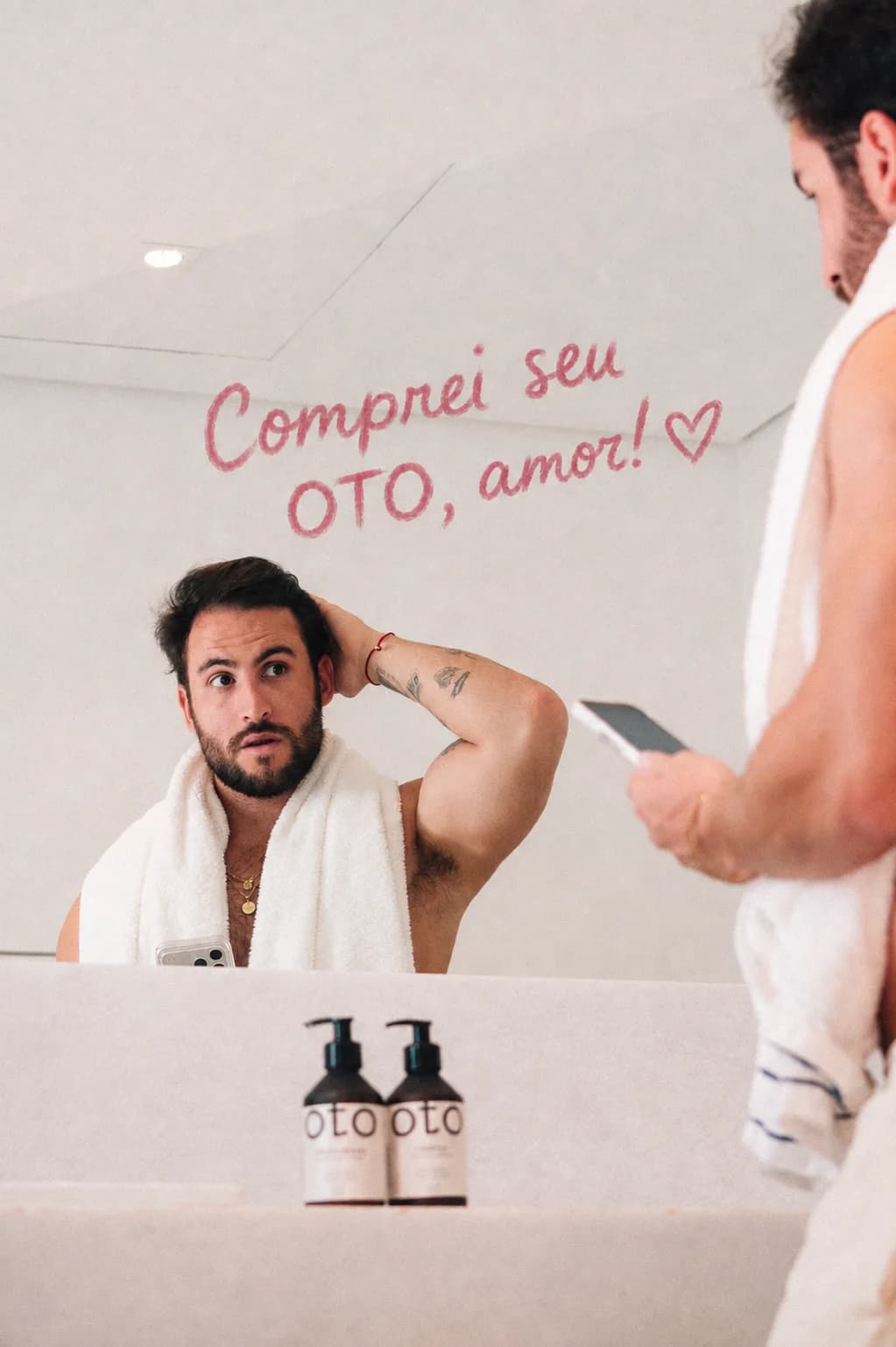 Homem diante do espelho do banheiro, com o recado “Comprei seu OTO, amor!” escrito de batom e o shampoo e o condicionador na bancada