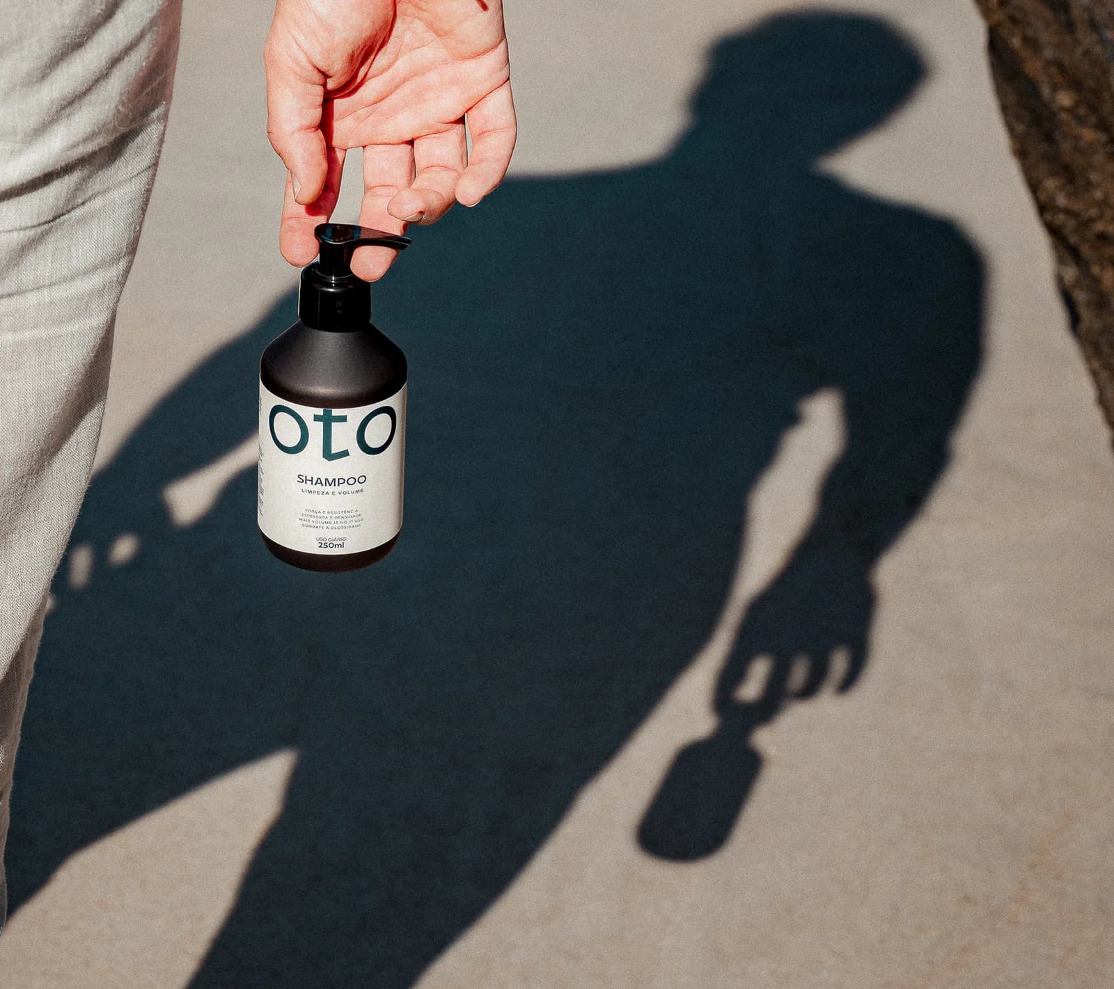 Homem caminhando ao sol com o shampoo OTO na mão e a sombra projetada no chão
